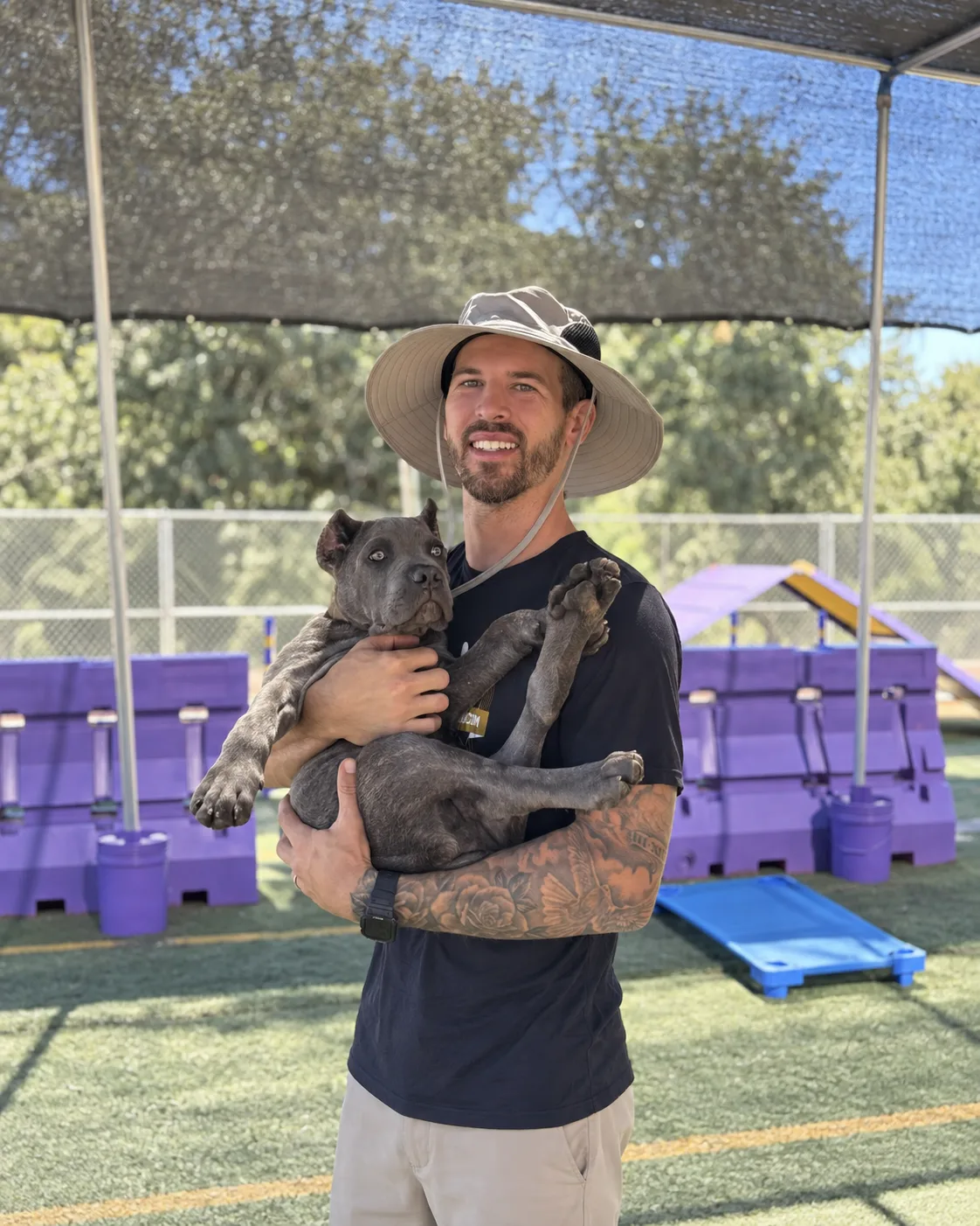 Joe from the EZ Pups crew, smiling under a wide-brim hat, holding a grey puppy