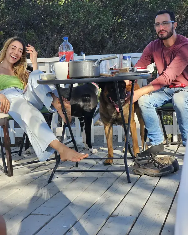 Andrew at the deck table with two dogs waiting underneath for scraps